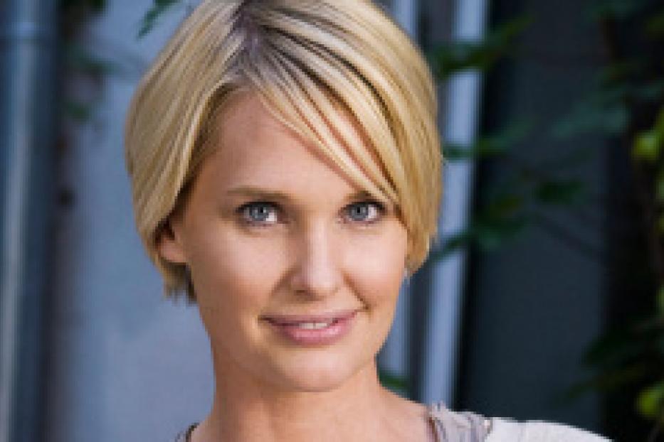 Eine Frau mit blonden, kinnlangen Haaren lächelt in die Kamera.