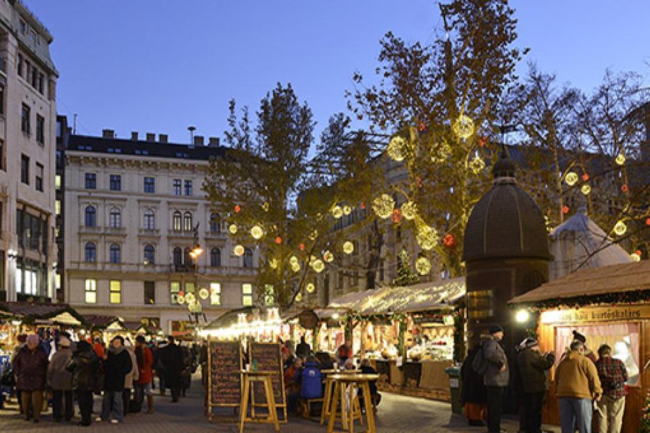 Ein Weihnachtsmarkt mit Buden und Menschen in einer Stadt bei Dämmerung.