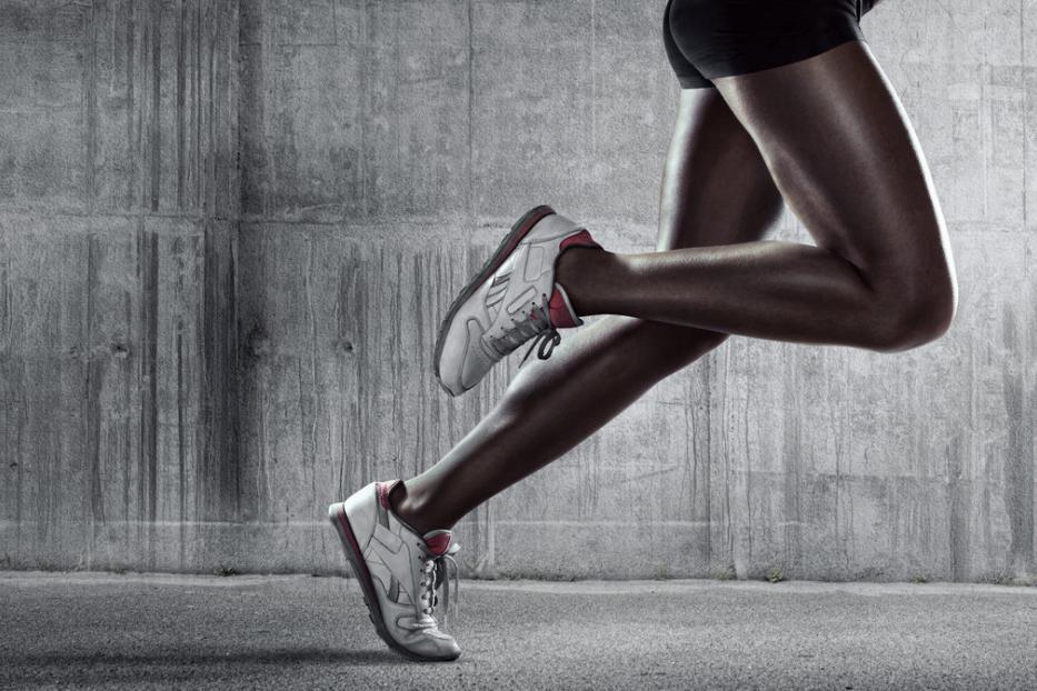 Die Beine eines Läufers in Bewegung vor einer grauen Betonwand.