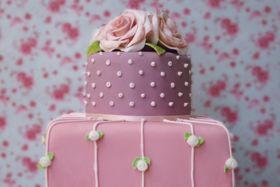 Ein zweistöckiger, rosa dekorierter Kuchen mit Rosen auf der Spitze.