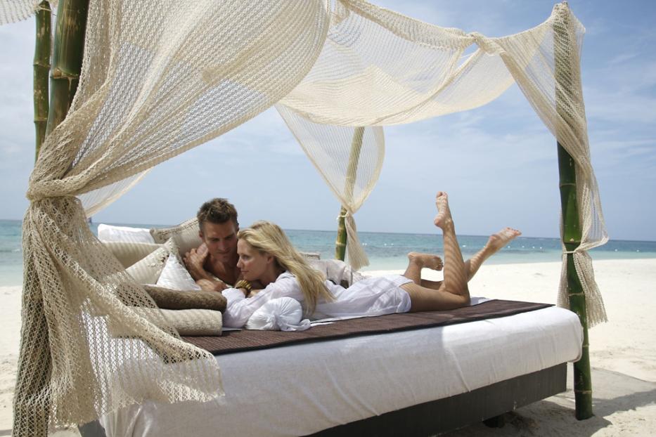 Ein Paar entspannt sich auf einer Liege mit Baldachin am Strand.