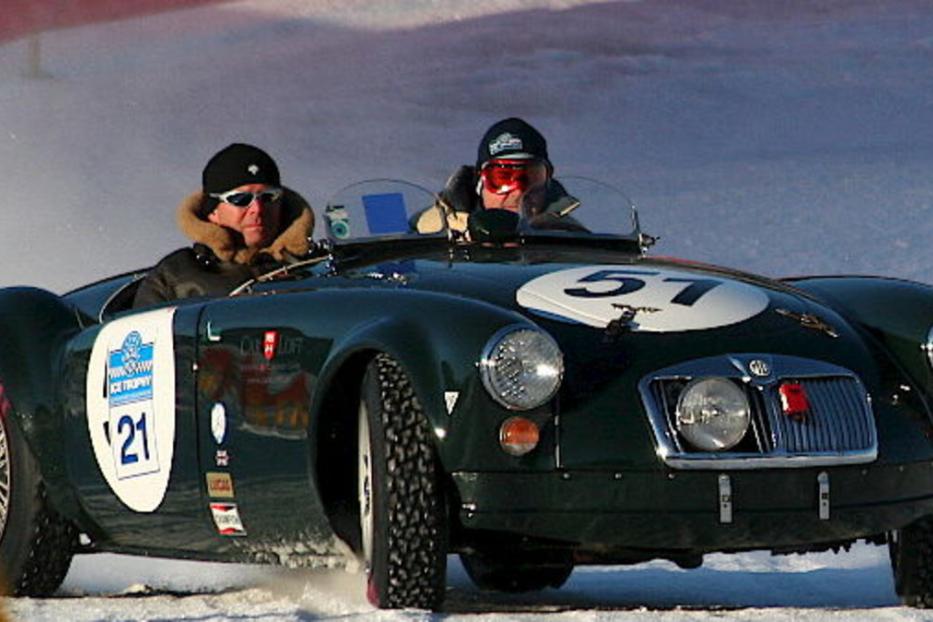 Zwei Männer fahren einen grünen Oldtimer bei einem Eisrennen.
