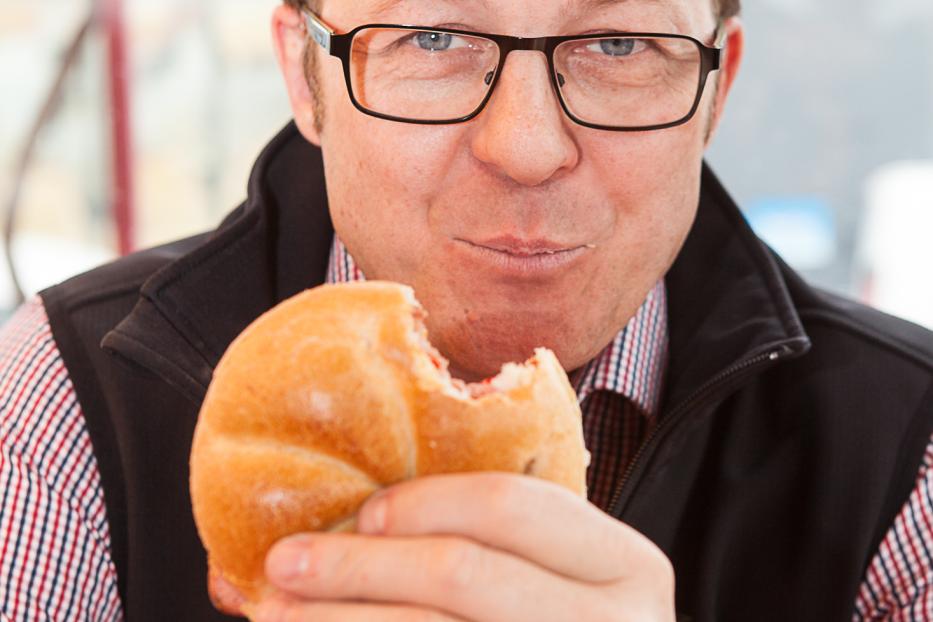 Ein Mann mit Brille isst ein Brötchen.