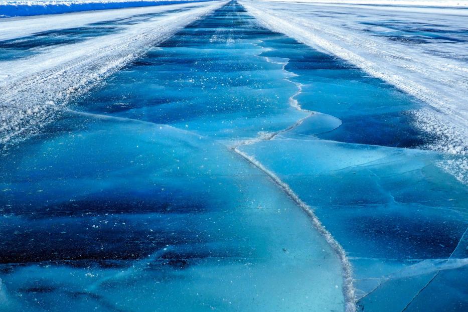 Eine gefrorene Straße mit Rissen im Eis führt in die Ferne.