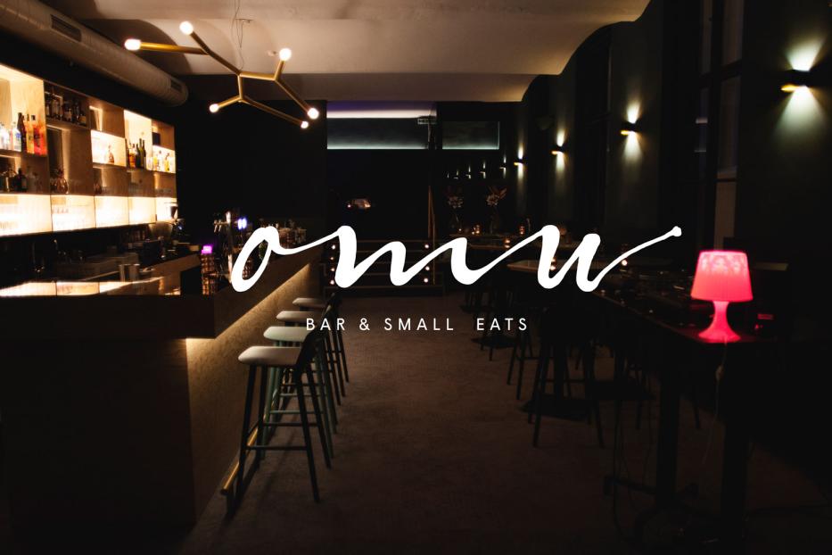 Innenansicht einer Bar mit Hockern an der Theke und Tischen mit roter Lampe.