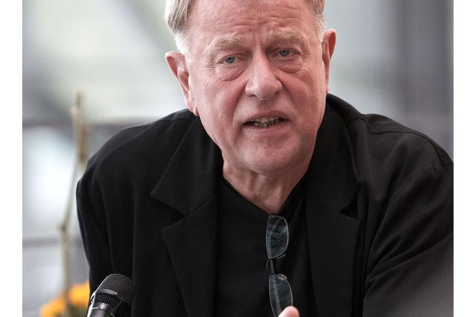 Ein Mann in einem schwarzen Jackett gestikuliert vor einem Mikrofon.