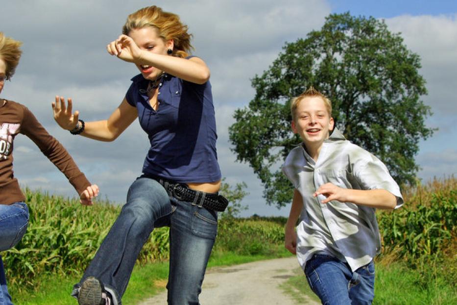 Drei Kinder rennen und springen auf einem Feldweg entlang.