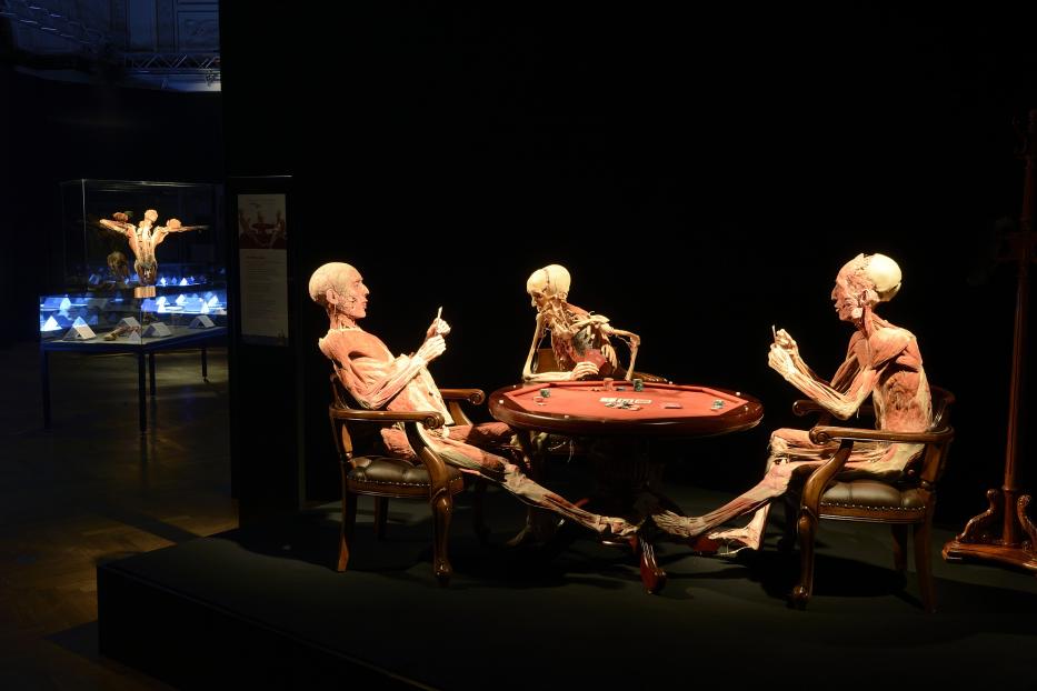 Drei menschliche Körper ohne Haut sitzen an einem Pokertisch.