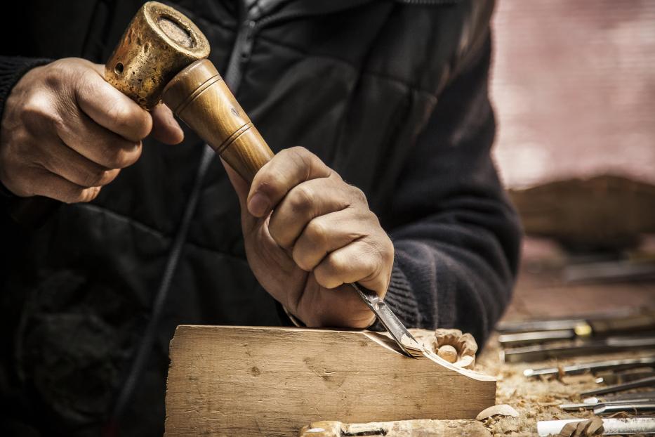 Ein Mann bearbeitet ein Stück Holz mit einem Stecheisen und einem Klopfholz.