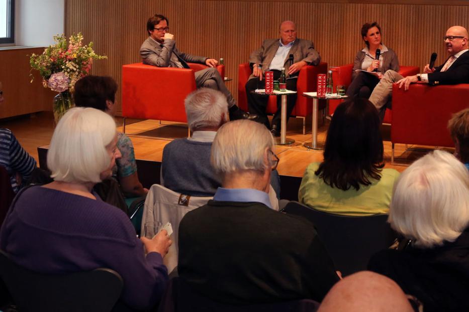 Eine Podiumsdiskussion mit vier Personen vor Publikum in einem Raum.