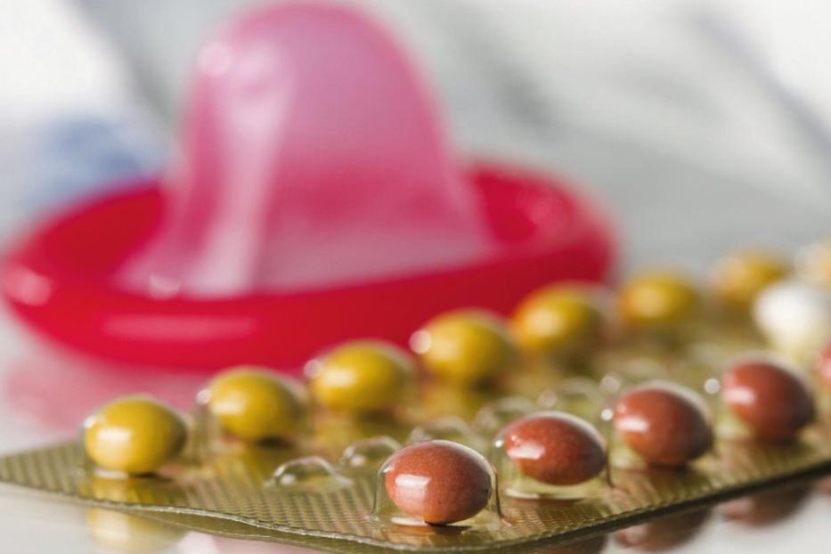 Ein Kondom und eine Blisterpackung mit Pillen liegen auf einem Tisch.