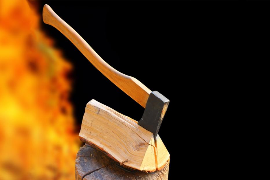 Eine Axt steckt in einem Holzscheit vor einem Hintergrund aus Flammen.