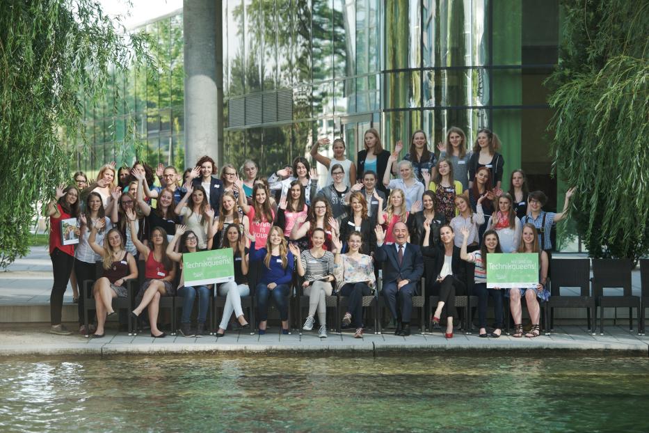 Eine große Gruppe junger Frauen und ein Mann posieren für ein Foto vor einem Gebäude und einem Teich.