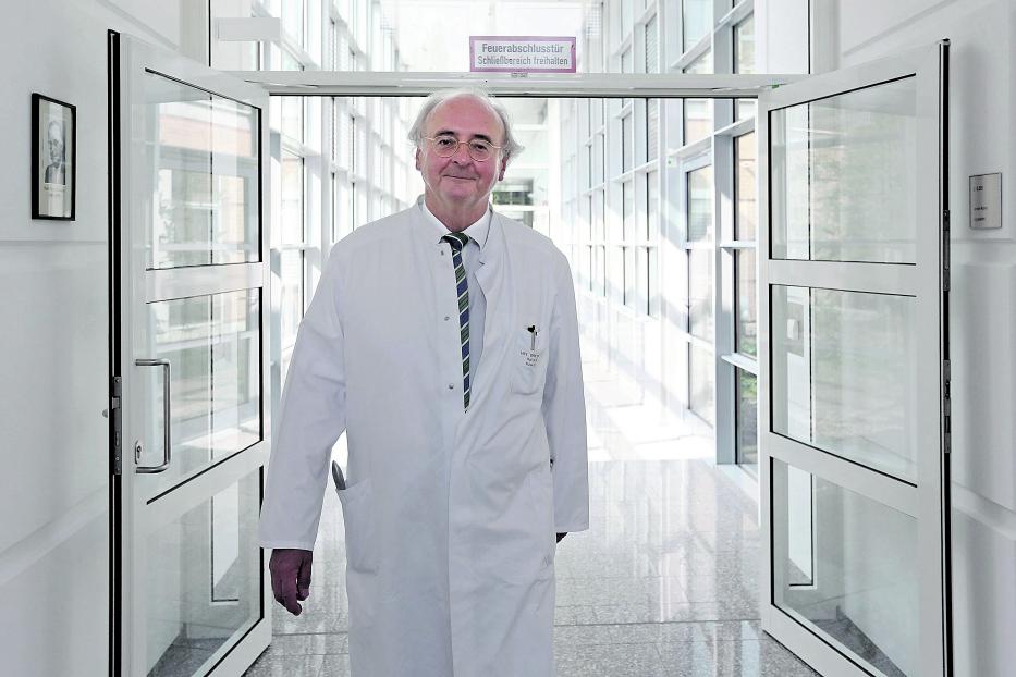 Ein Arzt in weißem Kittel steht in einem hellen Krankenhausflur.