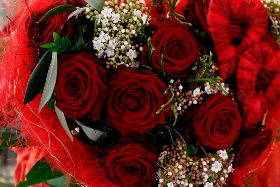 Ein Bouquet aus roten Rosen und kleinen weißen Blüten, umhüllt von rotem Ziergras.