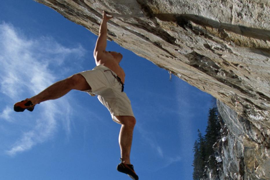 Ein Mann klettert an einer steilen Felswand unter blauem Himmel.