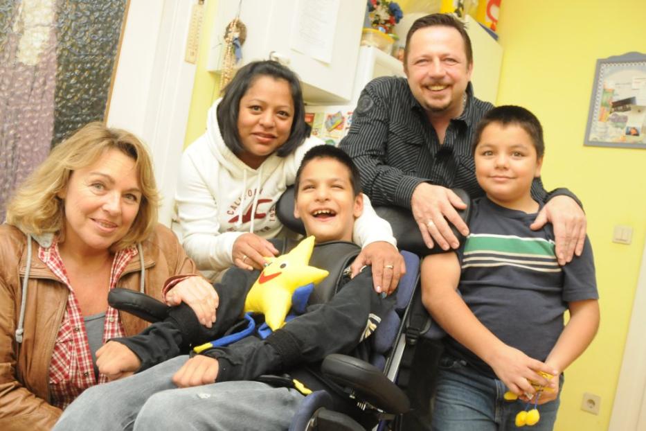 Eine Familie posiert für ein Foto in einem Wohnzimmer, ein Junge sitzt im Rollstuhl.
