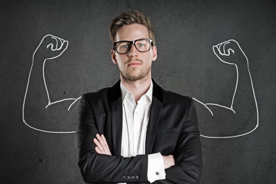 Ein Mann im Anzug steht vor einer Tafel mit aufgemalten Muskelarmen.