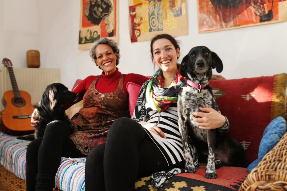 Zwei Frauen sitzen mit ihren Hunden auf einem Sofa in einem Wohnzimmer.