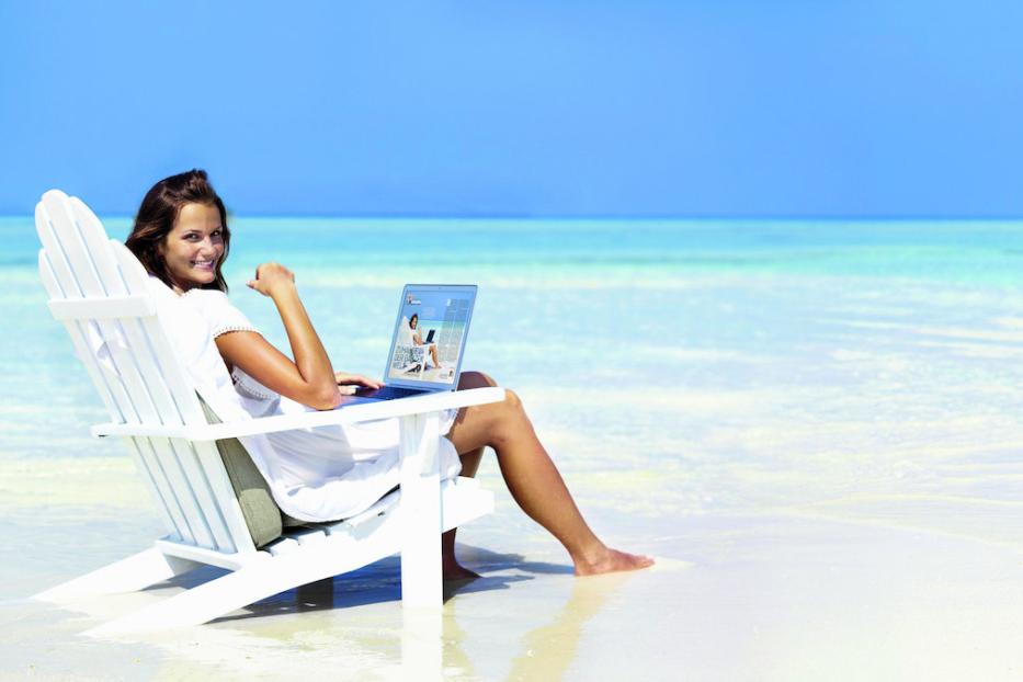 Eine Frau sitzt am Strand im Liegestuhl und arbeitet am Laptop.