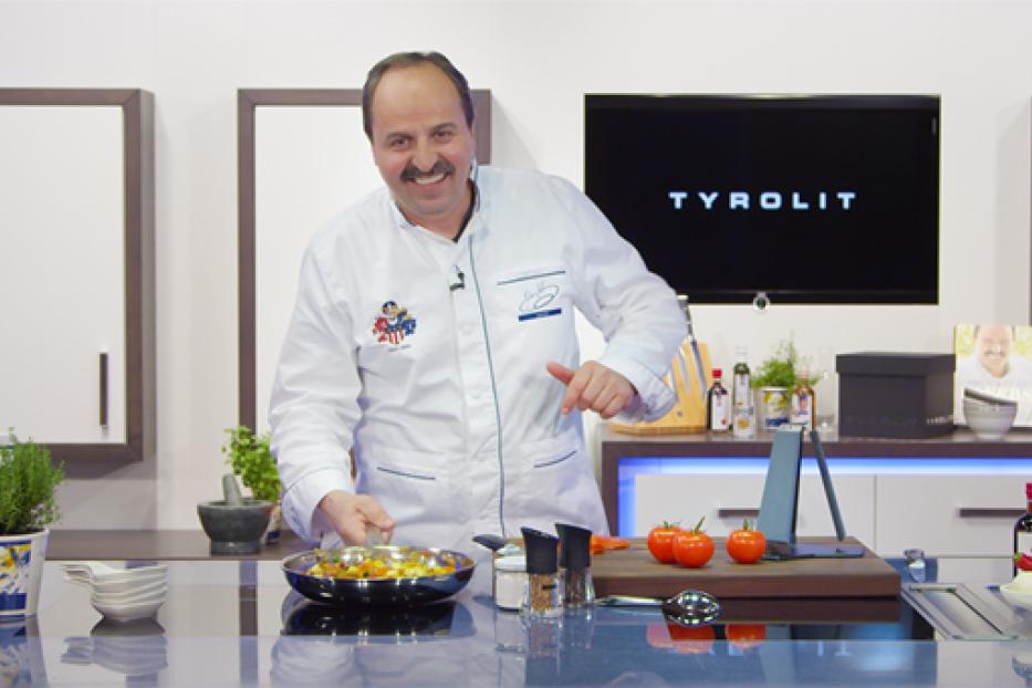 Ein Koch mit Kochjacke steht in einer Küche und bereitet eine Mahlzeit zu.