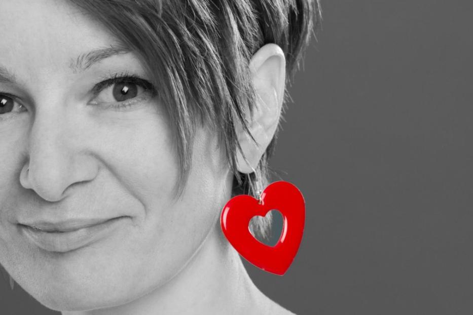 Eine Frau mit kurzem Haar trägt einen roten herzförmigen Ohrring.
