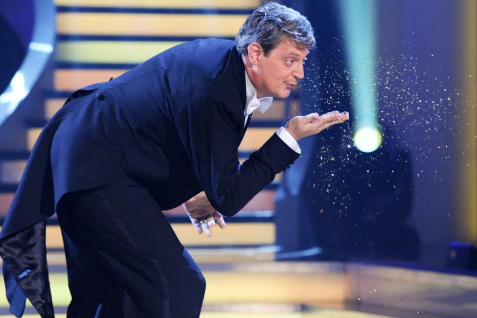 Ein Mann im Anzug bläst Glitzer von seiner Hand.