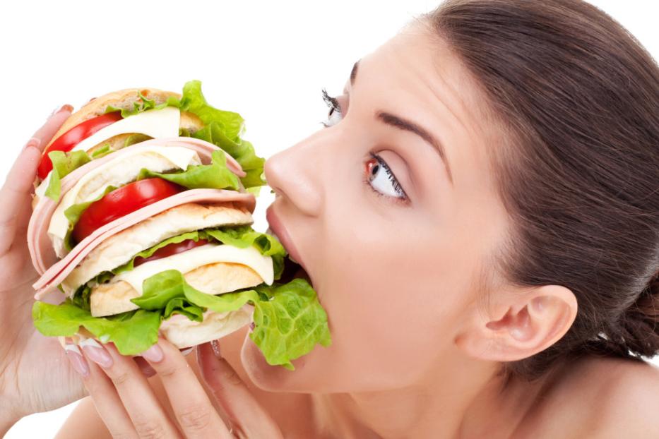 Eine Frau isst ein großes Sandwich mit Salat, Tomaten, Käse und Wurst.