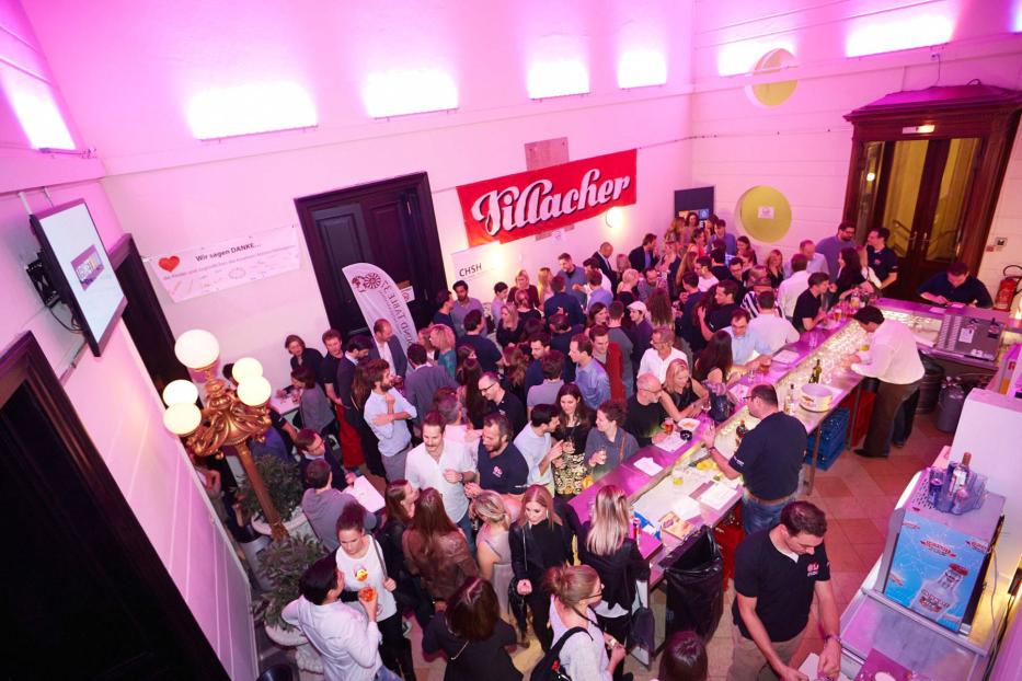 Viele Menschen versammeln sich in einer Bar unter einem „Villacher“-Banner.