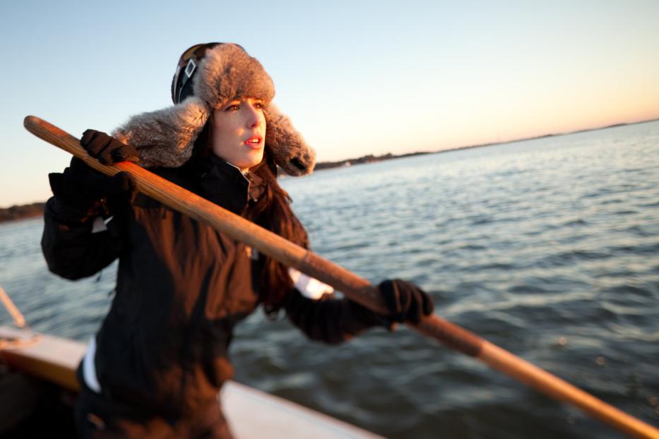 Eine Frau mit Pelzmütze rudert auf einem See bei Sonnenuntergang.