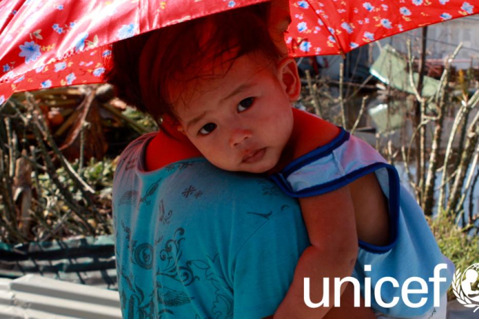 Ein Kind wird von einer Person unter einem roten Sonnenschirm getragen.