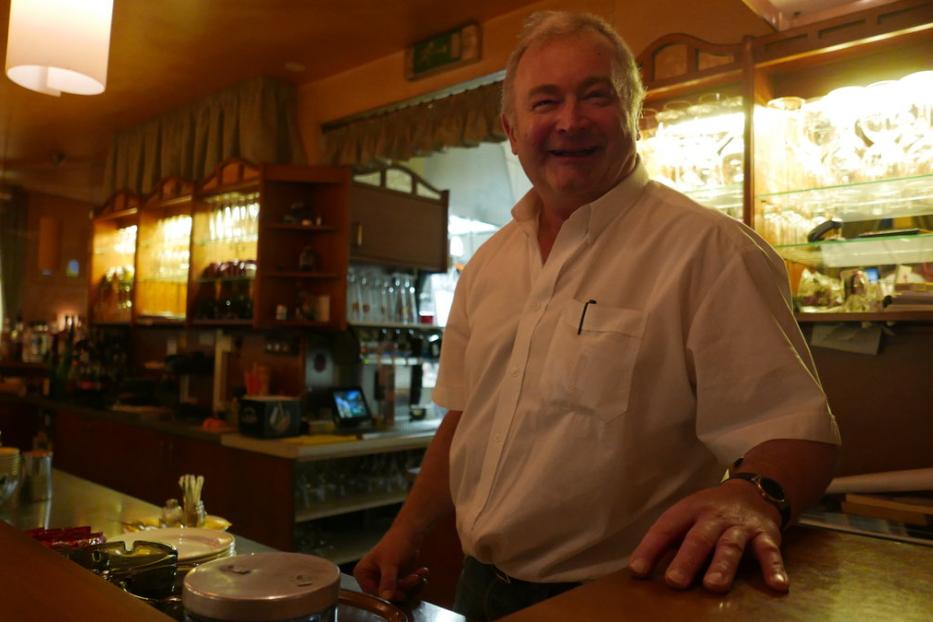 Ein lächelnder Mann steht hinter einer Bar.