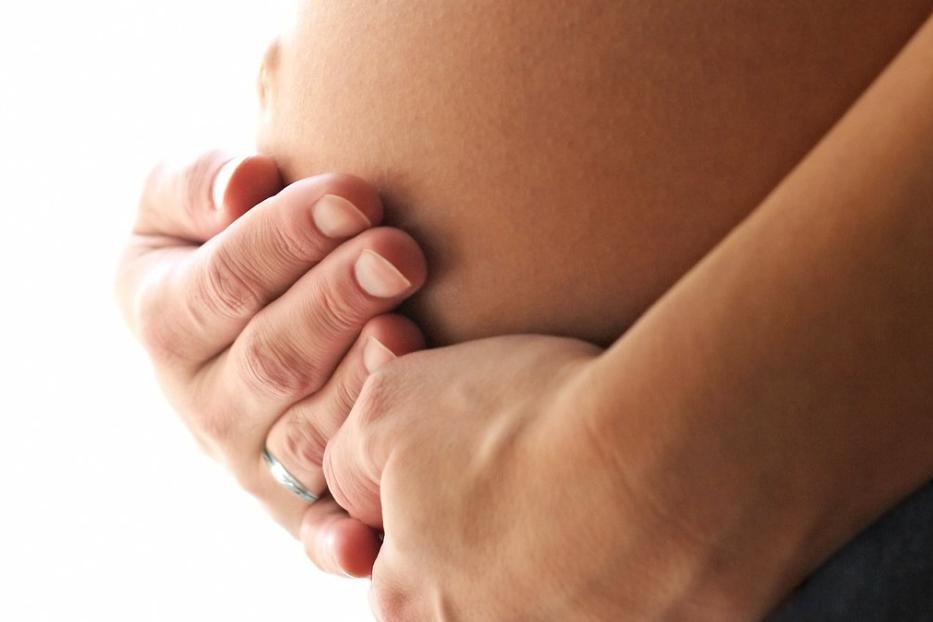 Eine Frau hält ihre Hände schützend um ihren Babybauch.
