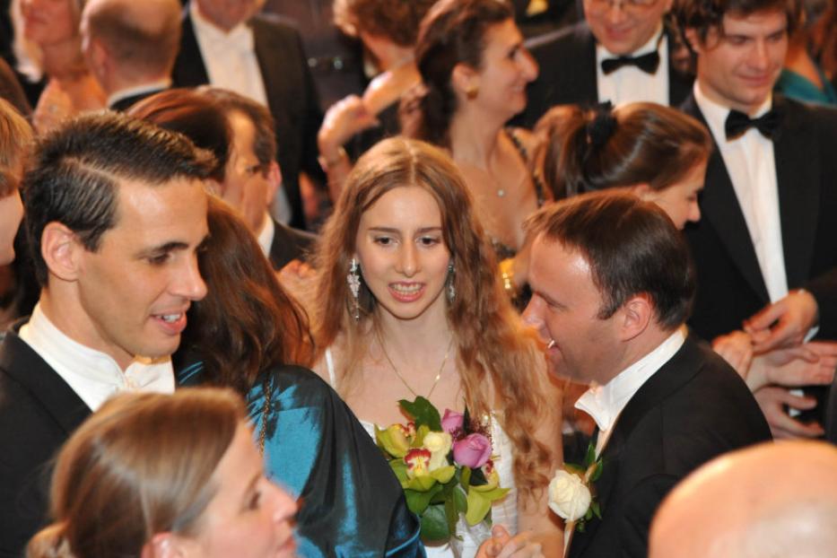 Eine junge Frau mit Blumenstrauß, umgeben von festlich gekleideten Gästen.