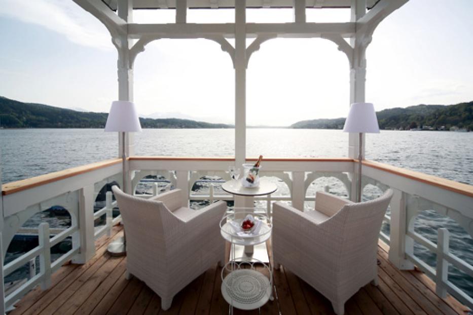 Ein Pavillon am See mit zwei Sesseln, einem Tisch und einer Flasche Champagner.