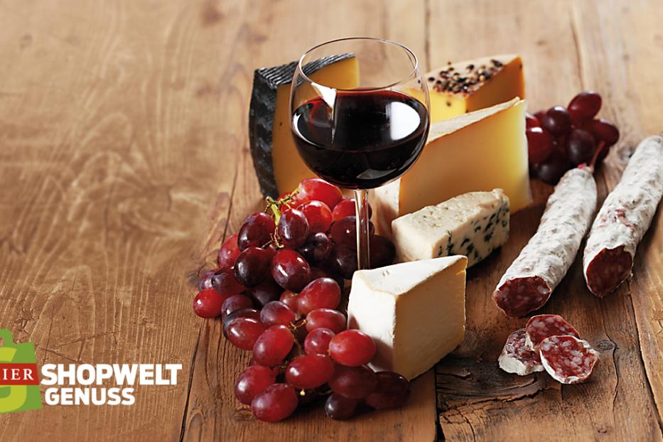 Arrangement aus Käse, Salami, Trauben und einem Glas Rotwein auf einem Holztisch.