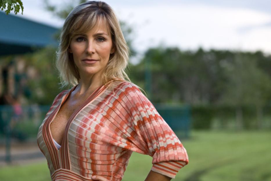 Eine Frau mit blonden Haaren posiert in einem gemusterten Kleid im Freien.