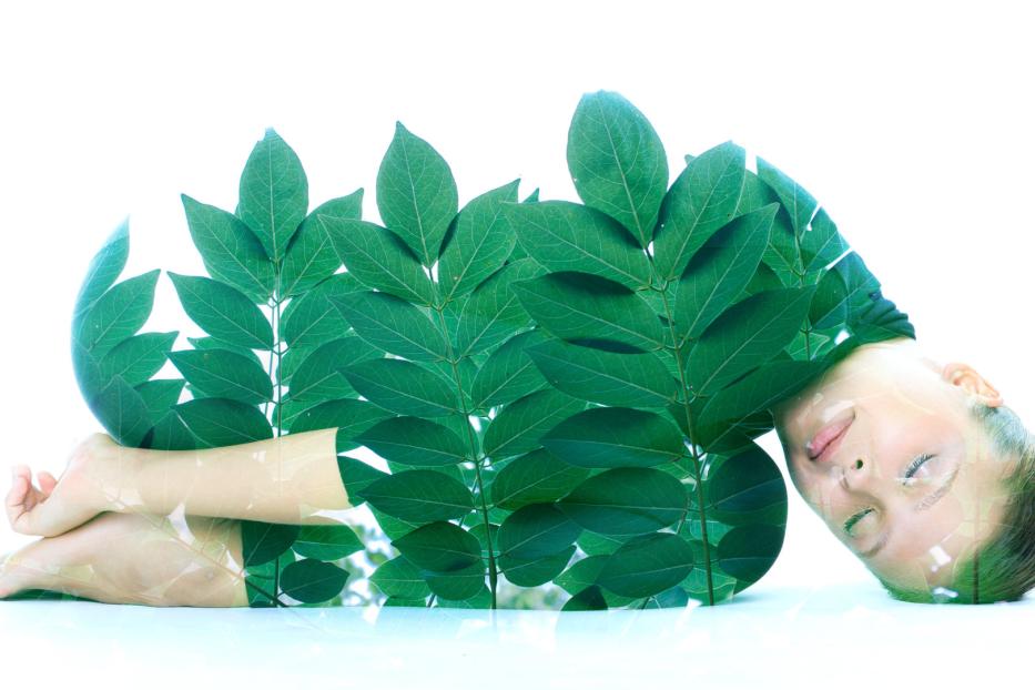 Eine Frau meditiert, überlagert mit dem Bild von grünen Blättern.