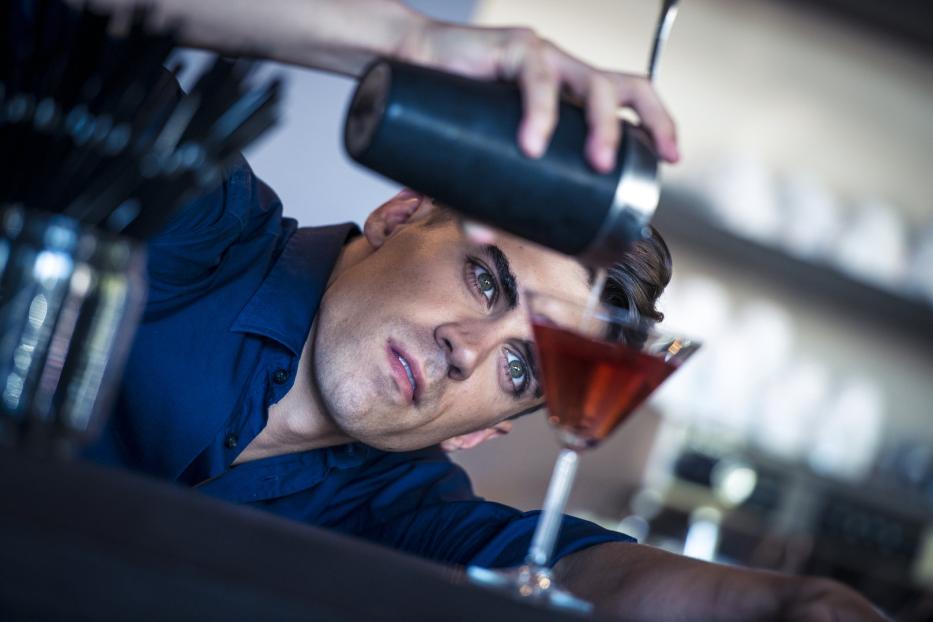 Ein Barkeeper gießt einen roten Cocktail in ein Martiniglas.