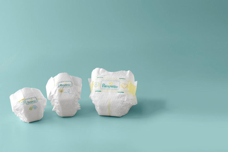 Drei Pampers-Windeln unterschiedlicher Größen auf hellblauem Hintergrund.