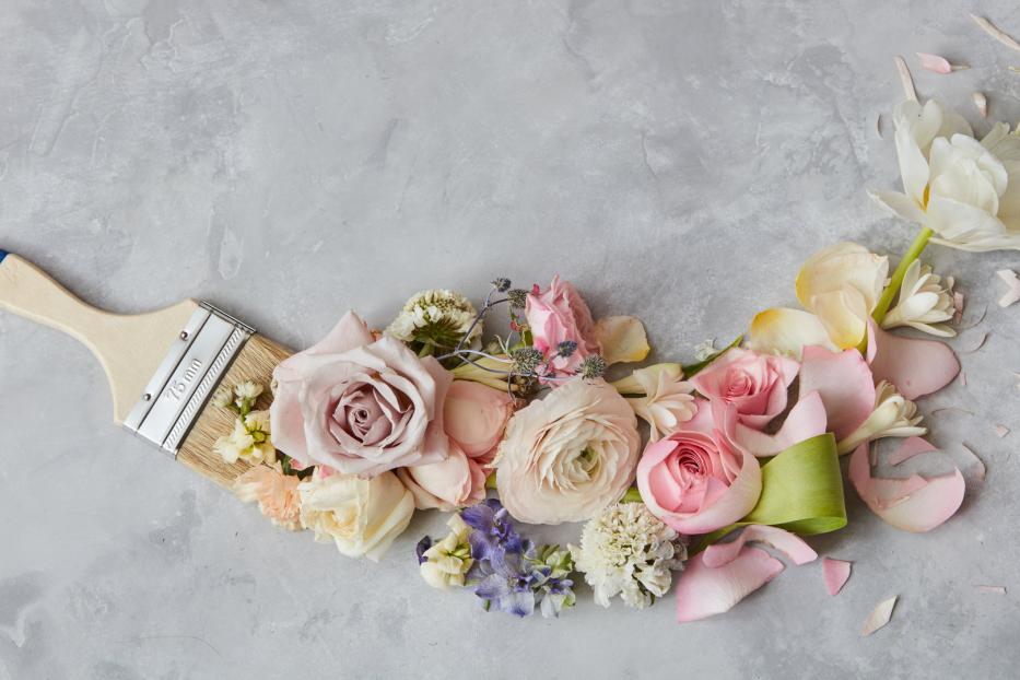 Ein Pinsel liegt auf einem grauen Untergrund, umgeben von verschiedenen Blumen.
