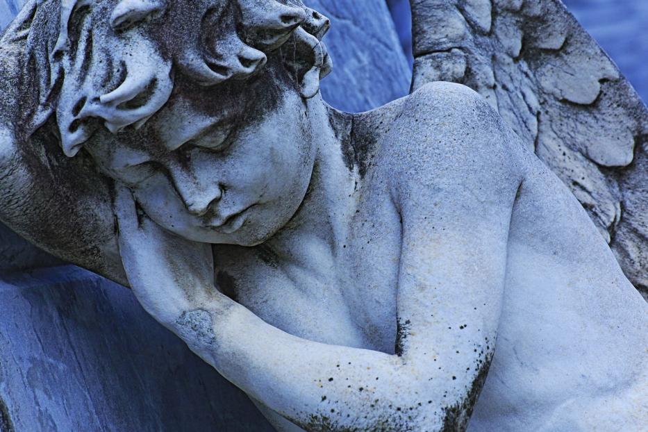 Die Skulptur eines liegenden, geflügelten Engels mit gesenktem Kopf.