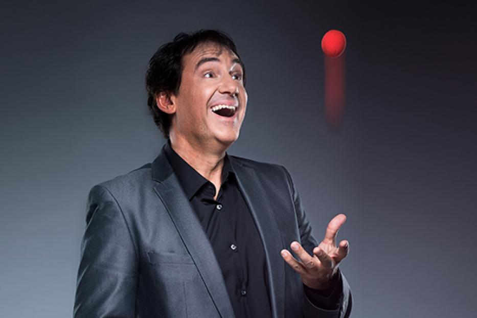 Ein Mann im Anzug jongliert mit einem roten Ball.