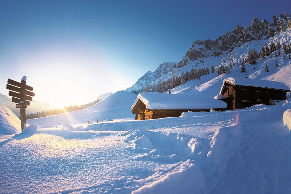 Eine verschneite Hütte in den Bergen bei strahlendem Sonnenschein.