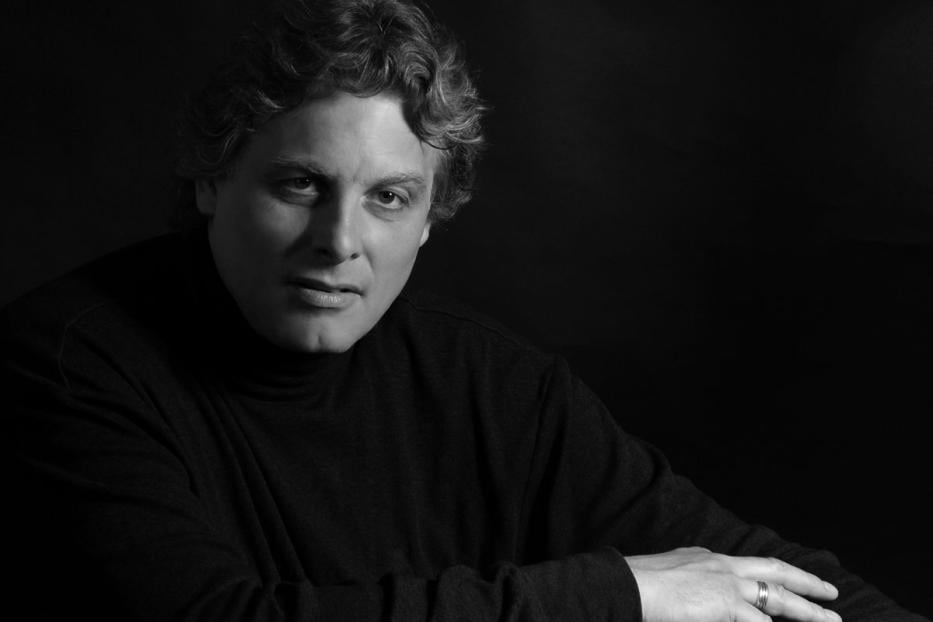 Ein Mann mit lockigem Haar und einem schwarzen Rollkragenpullover blickt in die Kamera.