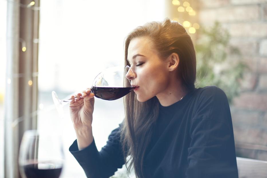 Frau trinkt Rotwein aus langstieligem Glas