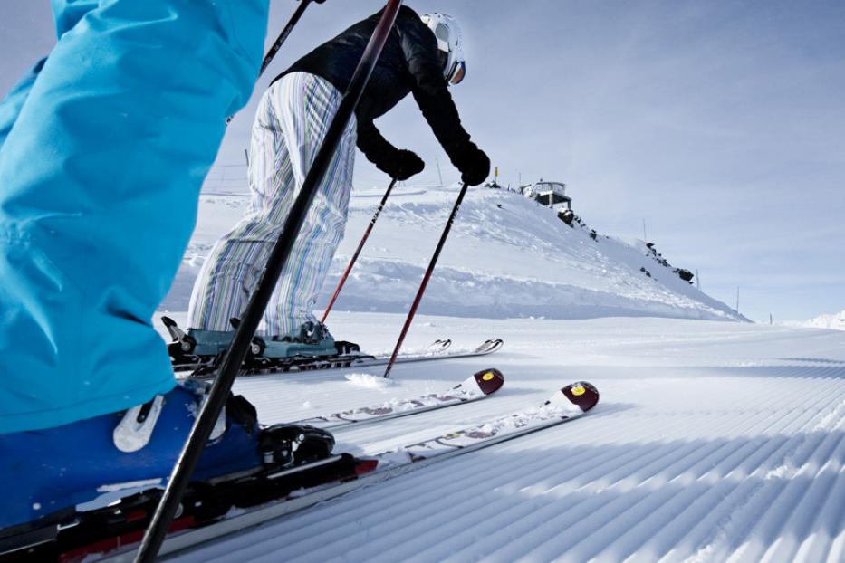 Skifahrer stehen auf einer präparierten Piste mit einem Gebäude im Hintergrund.