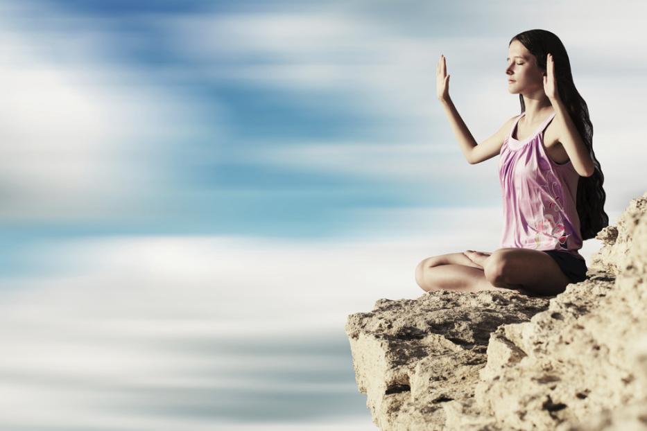 Eine Frau meditiert auf einer Klippe mit Blick auf den Himmel.