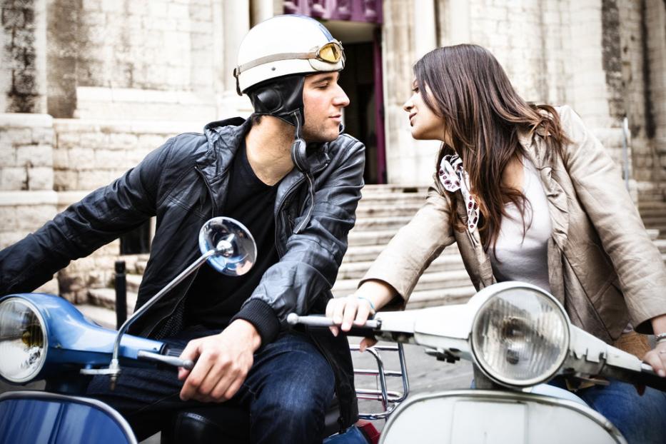 Ein Paar sitzt auf zwei Motorrollern und schaut sich an.