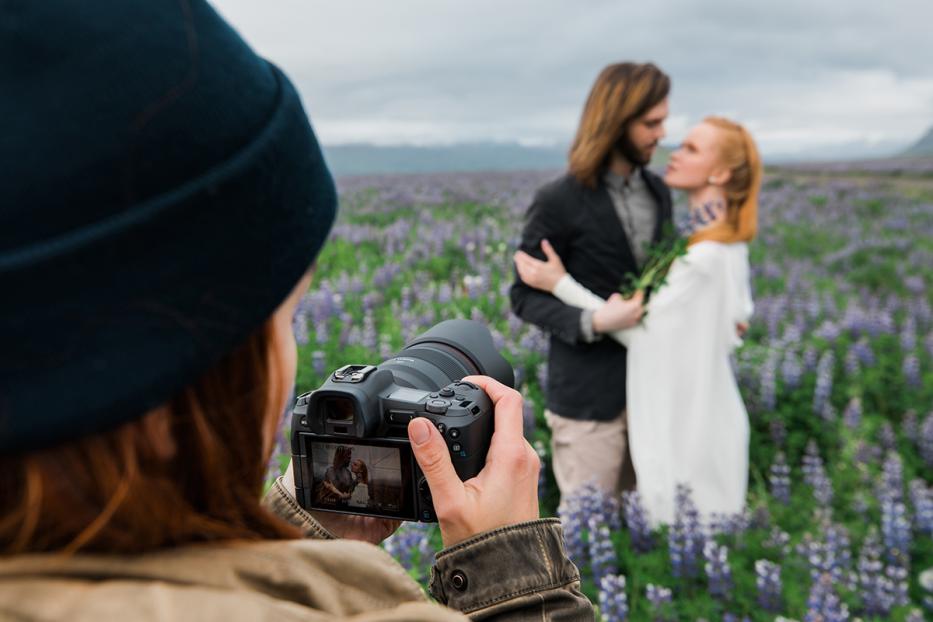 Eine Fotografin macht ein Foto von einem Paar in einem lila Blumenfeld.